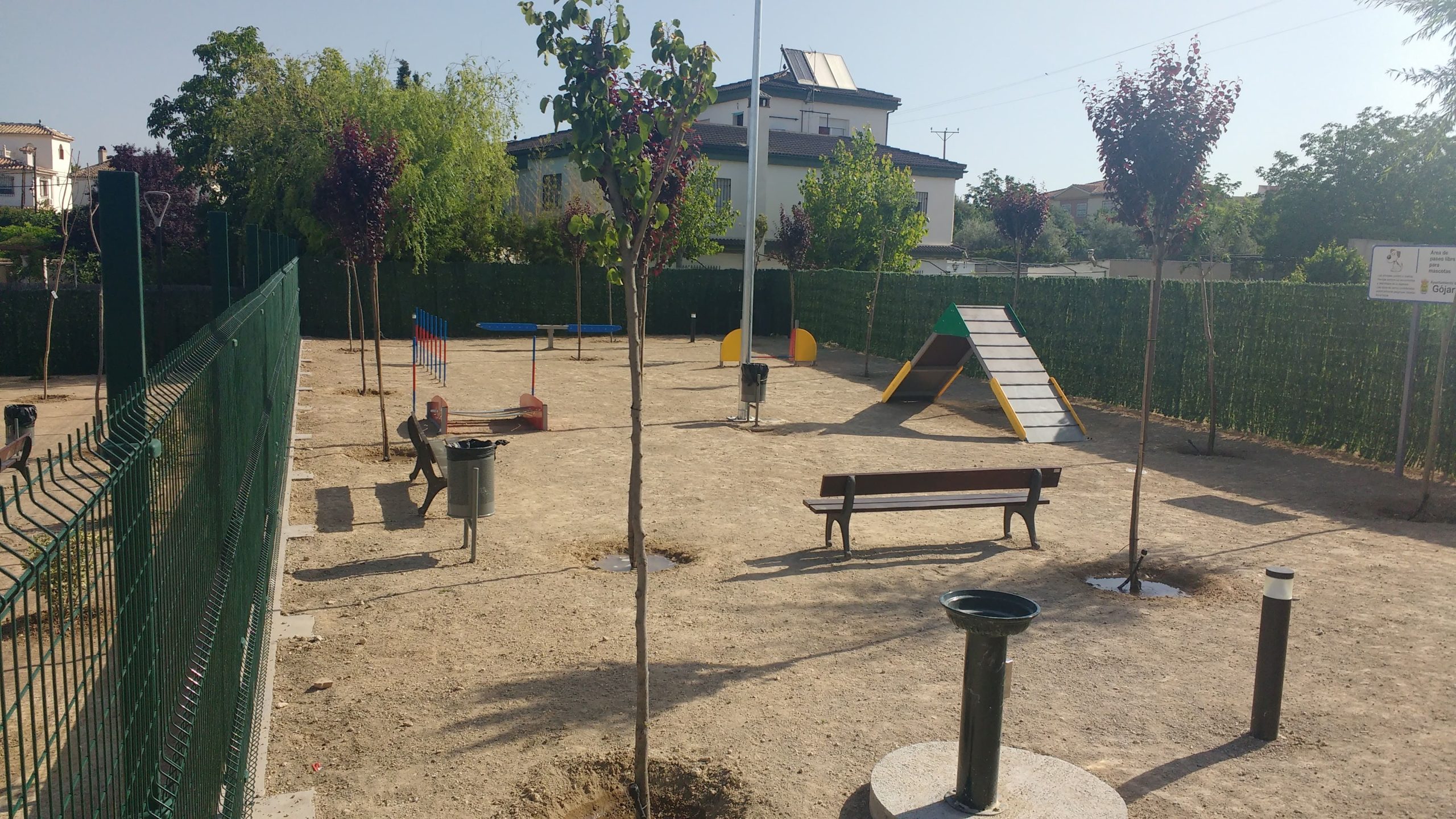 Parque canino de arena con columpios y una pirámide de cuerdas.