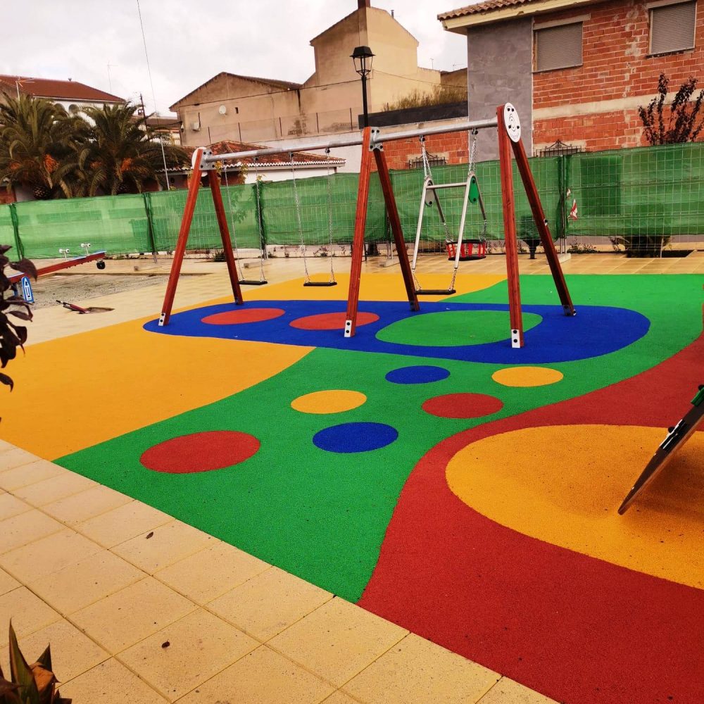 Área de juegos infantiles con suelo de caucho multicolor y columpios.