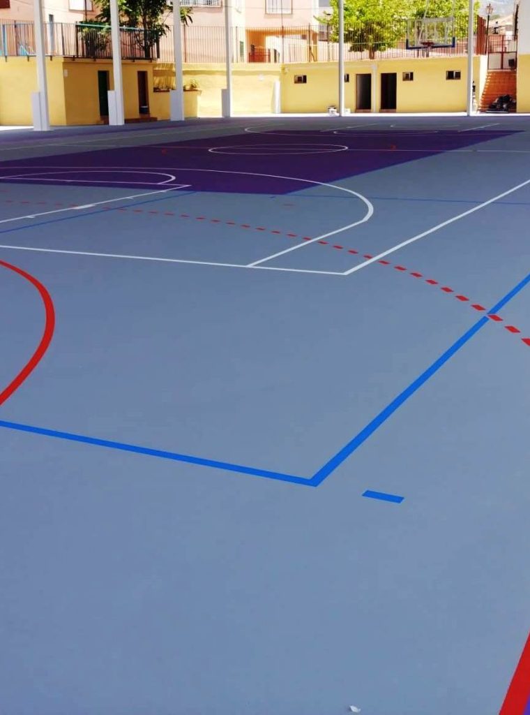 Cancha de deportes múltiples con superficie de color gris y líneas de demarcación para diferentes juegos.